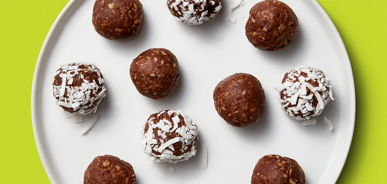 Rolled up banana balls coated in chocolate and coconut flakes are spaced out onto a white plate.