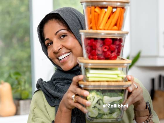 Zehra stands in kitchen laughing with reusable containers of fresh veggies and fruit in front of her.
