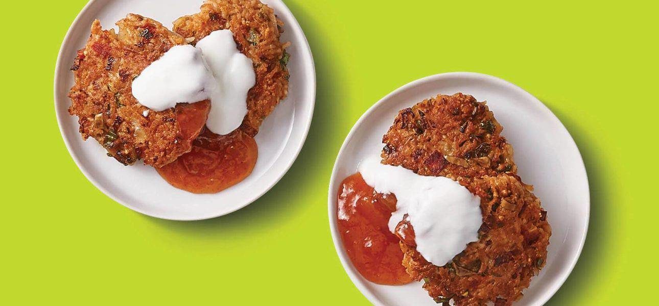 Two plates are filled with crisp and golden khichdi patties, topped with hearty spoonfuls of yoghurt and chutney.