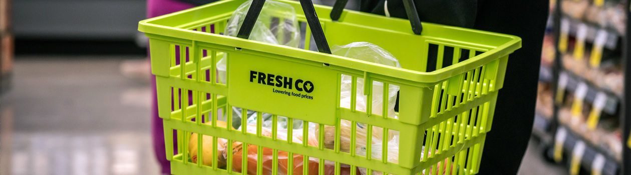 An image contains a person carrying a bright green shopping basket with the "FRESHCO" logo. The background features store shelves.