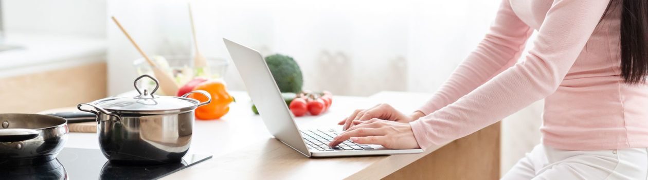 A Woman typing on her computer on a kitchen countertop