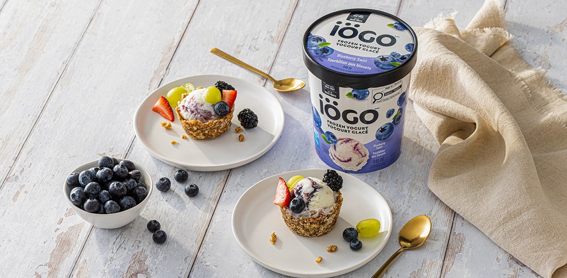 Two plates each hold a single iÃƒâ€“GO Blueberry Swirl Frozen Yogurt Mini Granola Tart, with a small bowl of fresh blueberries nearby.